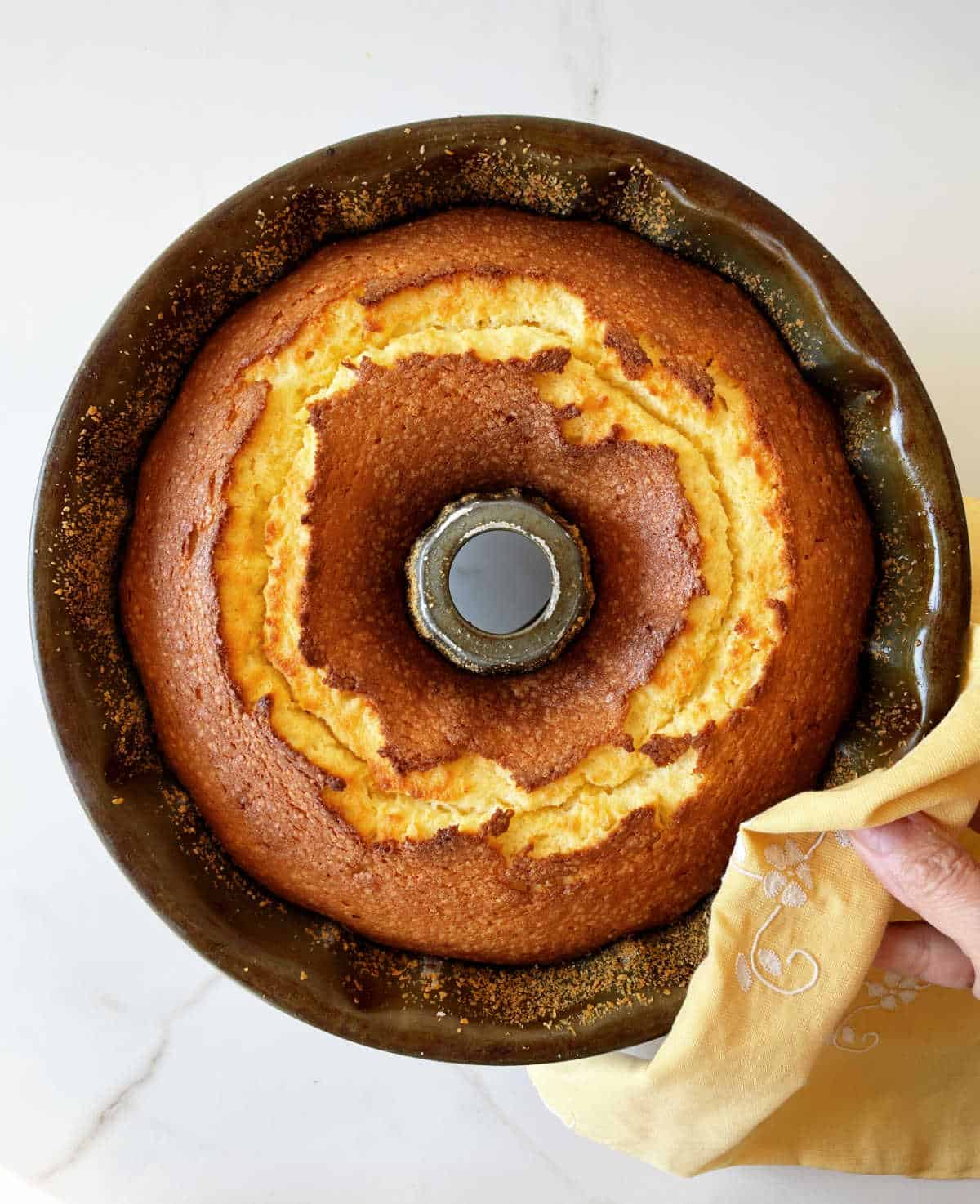 Top view of baked bundt cake in metal pan on white surface, yellow napkin