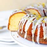 Lemon bundt cake with glaze and cut slice on white cake stand, beige background