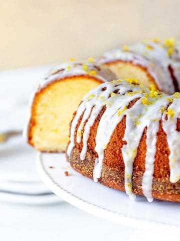 Lemon bundt cake with glaze and cut slice on white cake stand, beige background