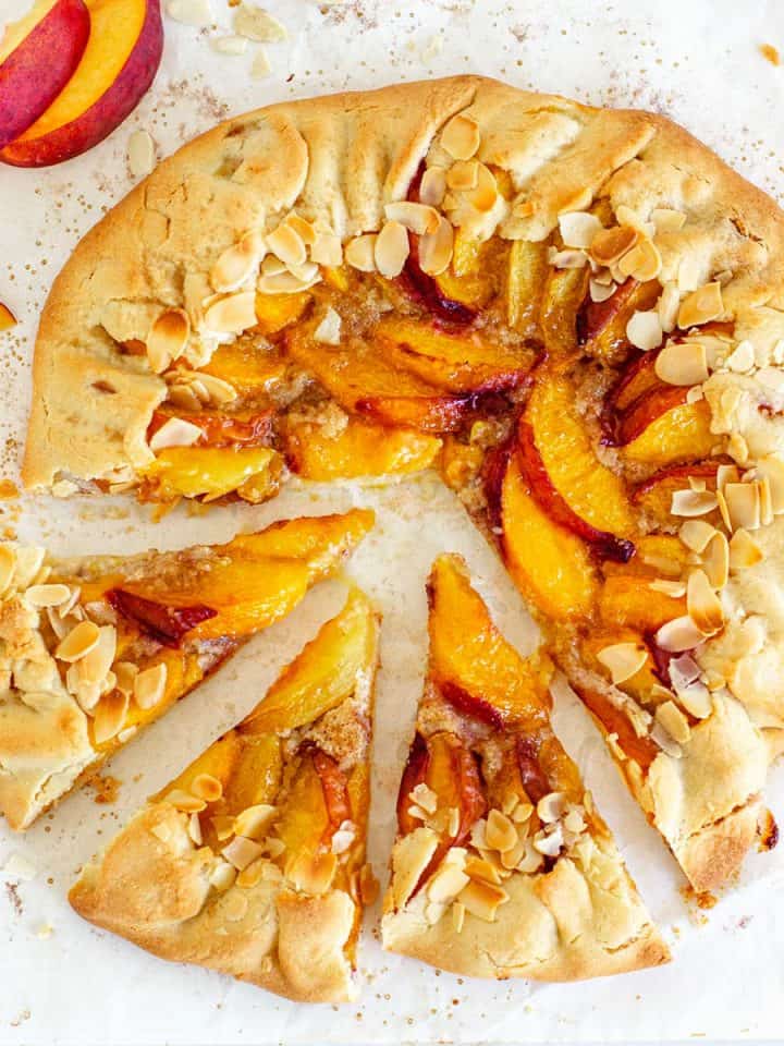 Whole baked peach galette on parchment paper; top view image.