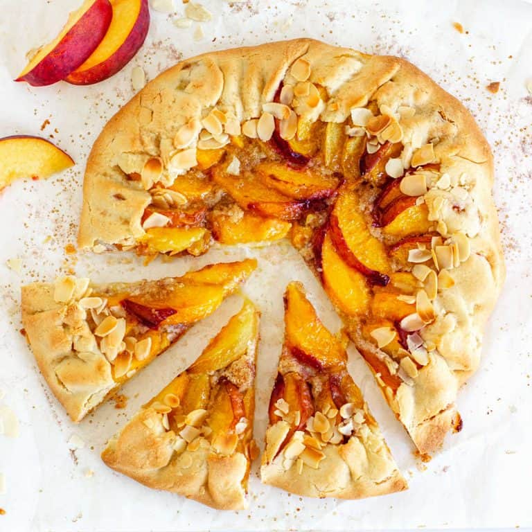 Whole baked peach galette on parchment paper; top view image.