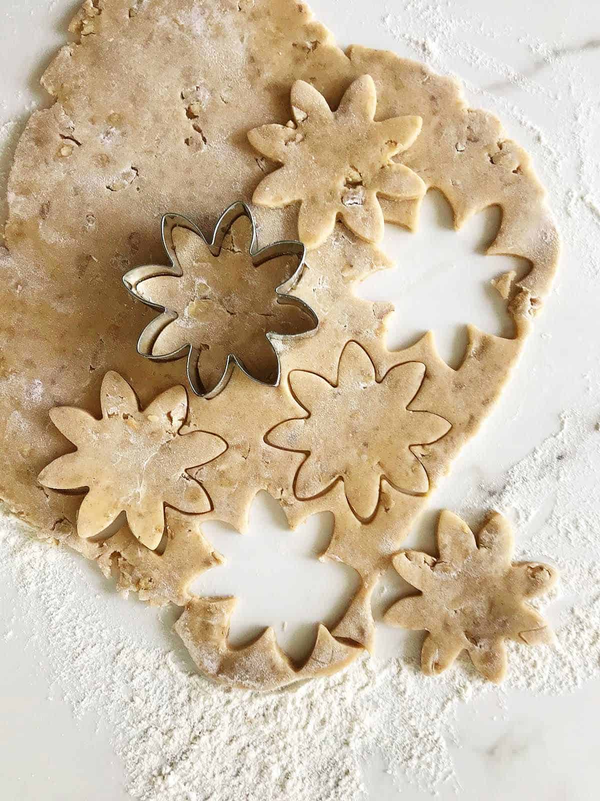 Rolled cinnamon dough cut into flowers, cookie cutter, white marble surface