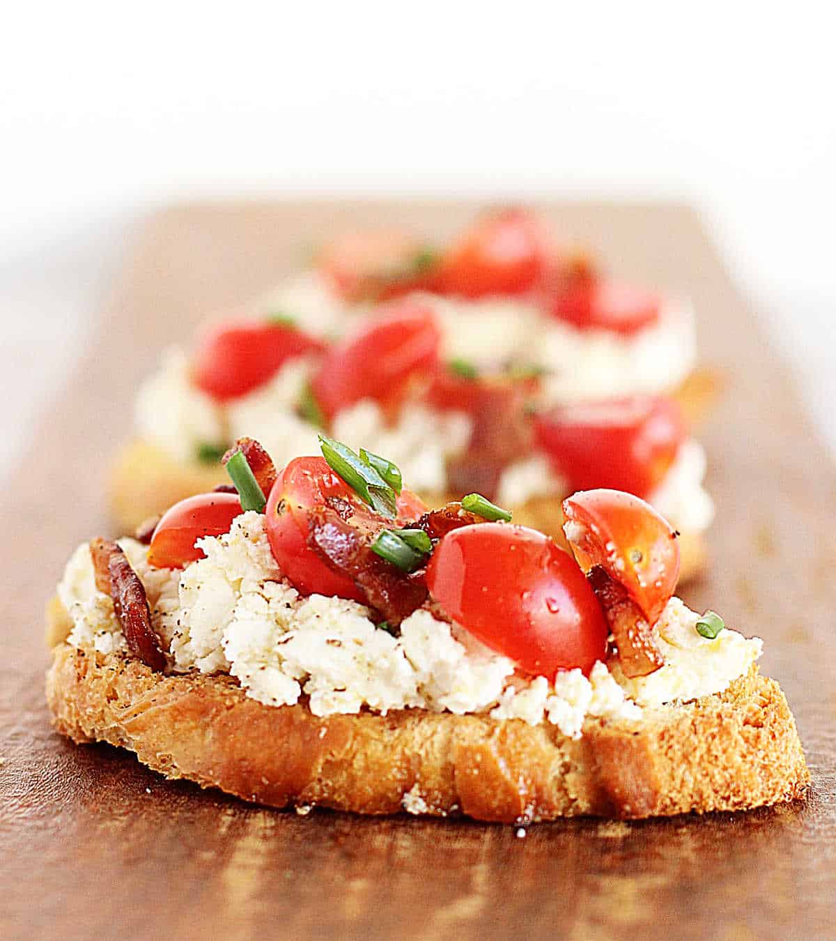 Long wooden board with row of ricotta tomato toast