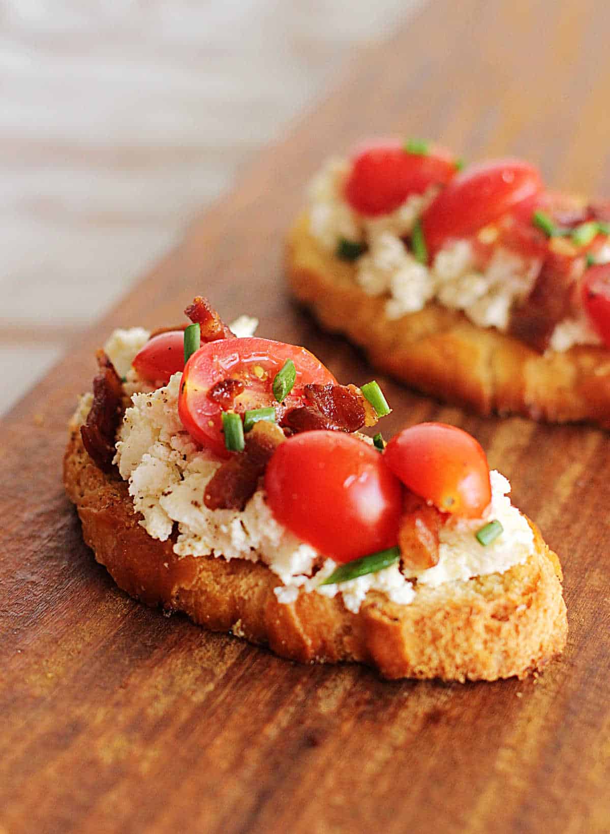 Two slices of ricotta toast wit tomatoes and bacon on wooden board