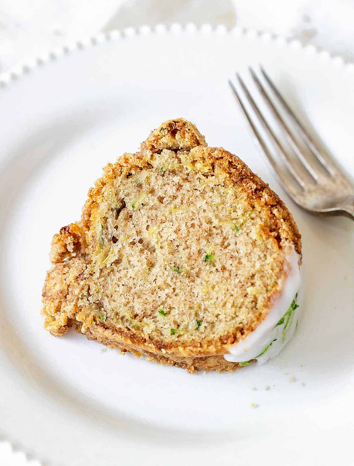 Slice of zucchini bundt cake on white plate with silver fork