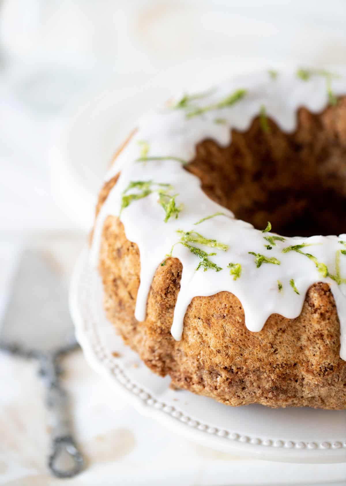 Top view of partial glazed bundt cake on white cake stand, silver cake server.