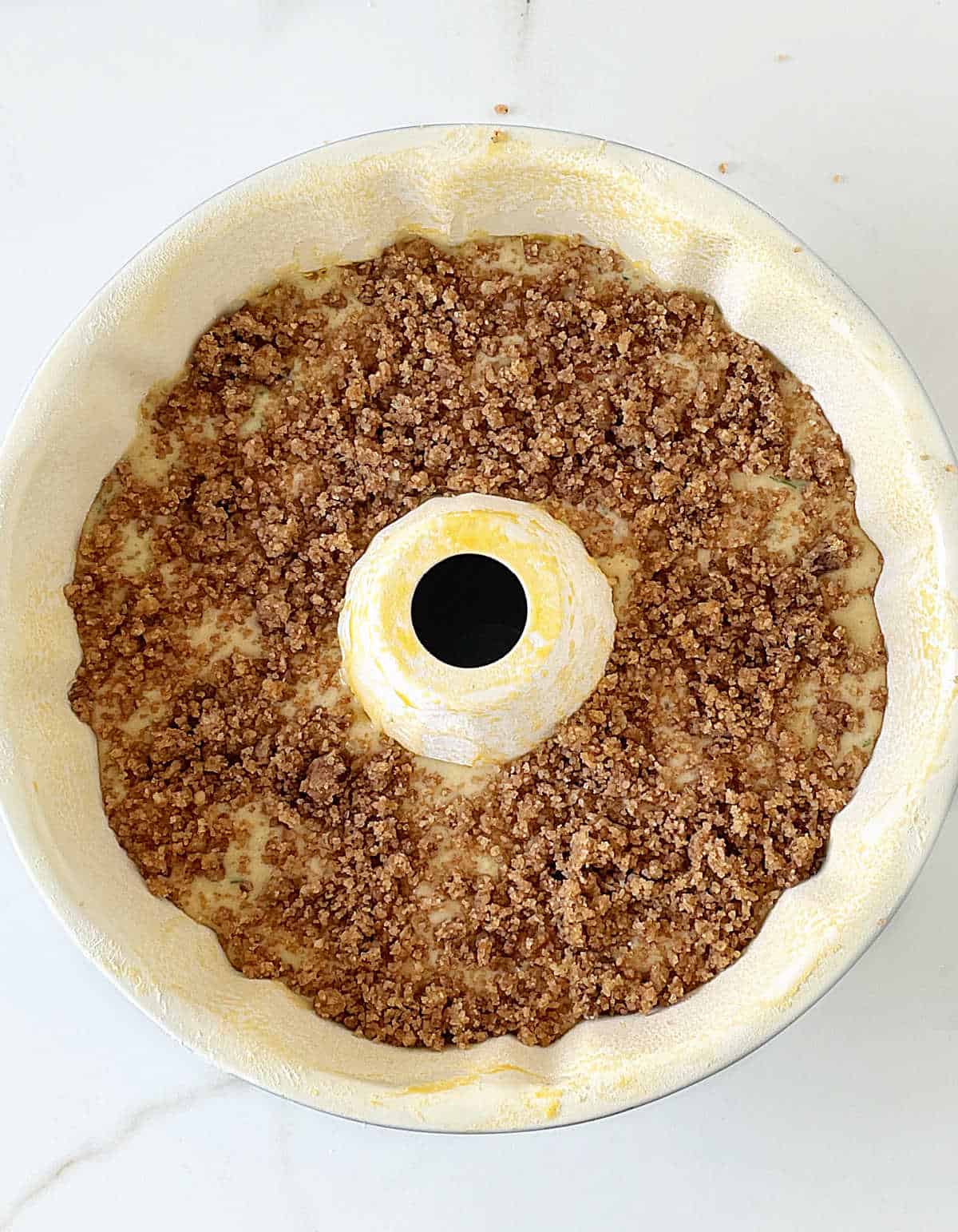 Overview of bundt cake pan with crumble on top on white surface.