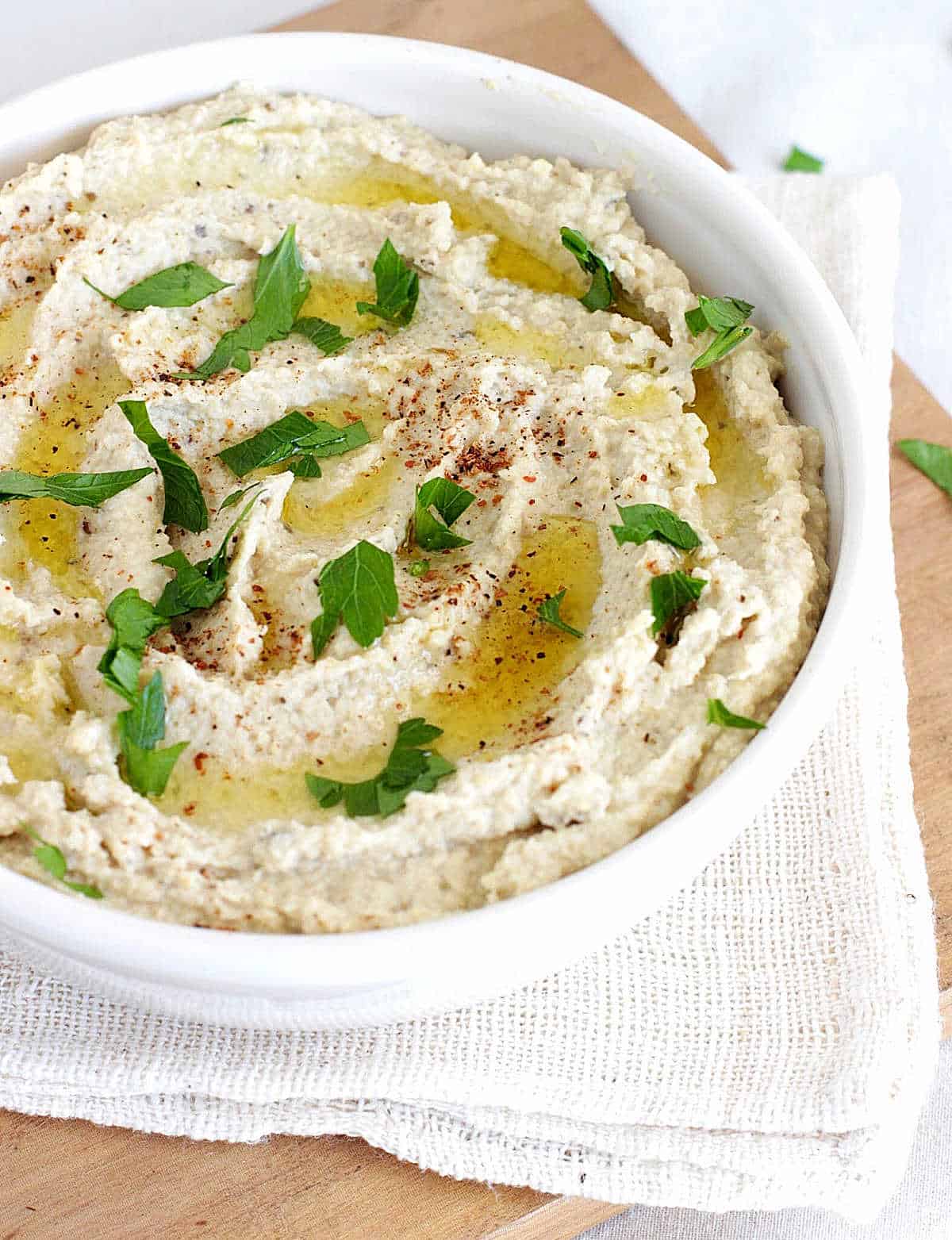 White napkin with white bowl containing hummus with parsley garnish on top 