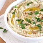White bowl with eggplant hummus, sprinkled with parsely and olive oil, on wooden board