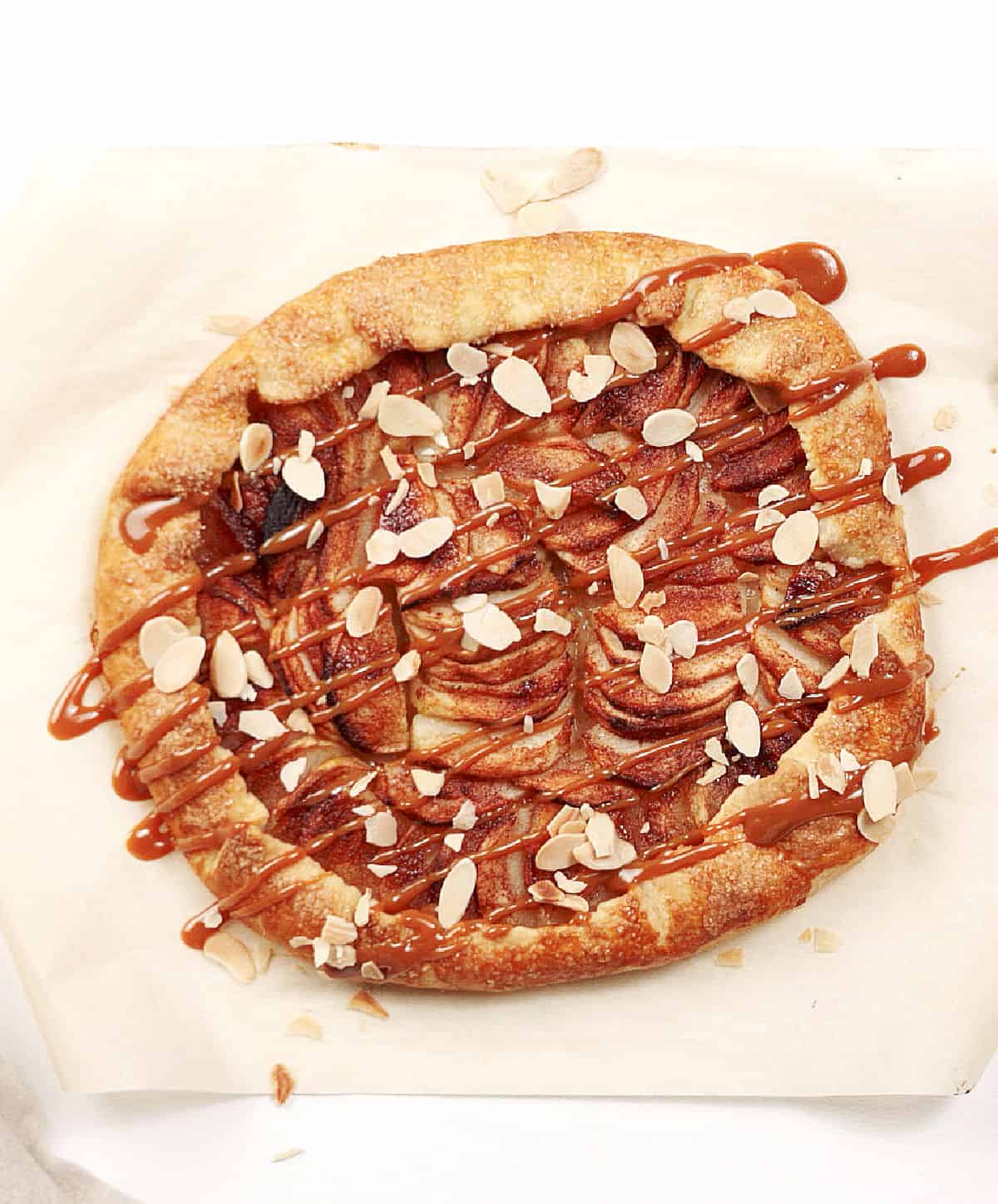 White surface with whole apple galette with caramel on parchment paper