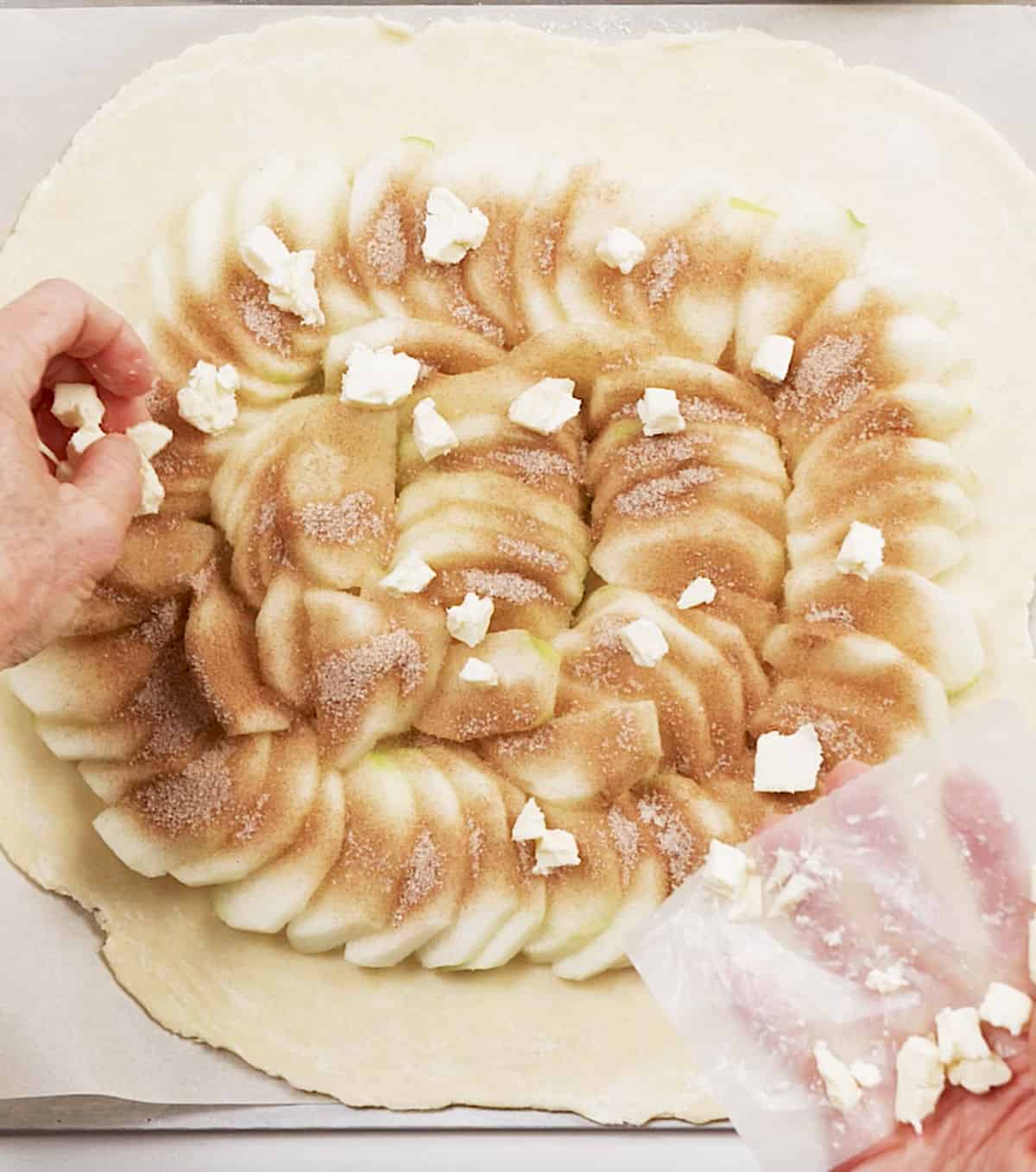 Adding small butter pieces to apples with cinnamon sugar on top of flat pie crust