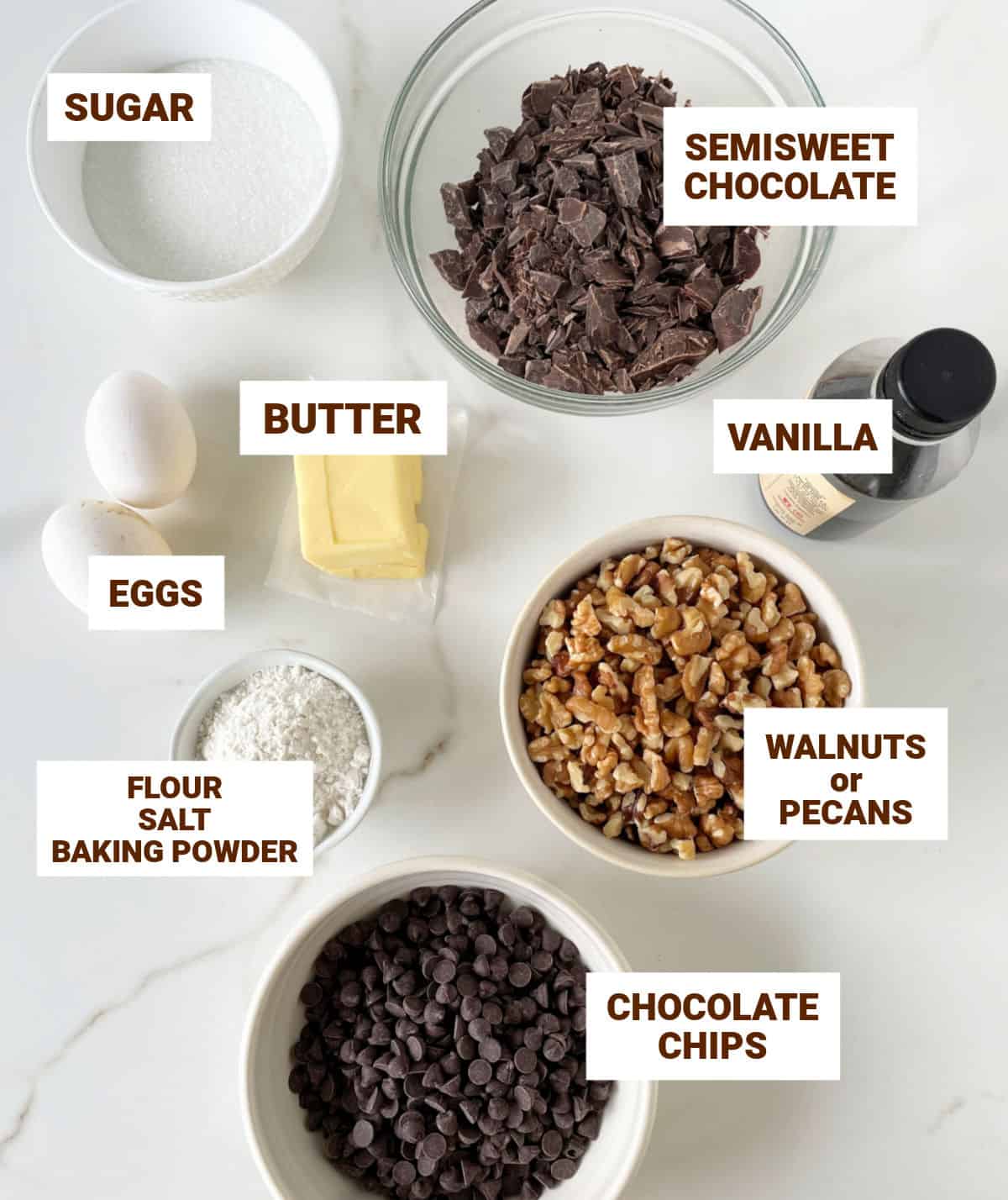 White surface with bowls containing ingredients for chocolate walnut cookies including butter, eggs, chopped chocolate and chips, vanilla.