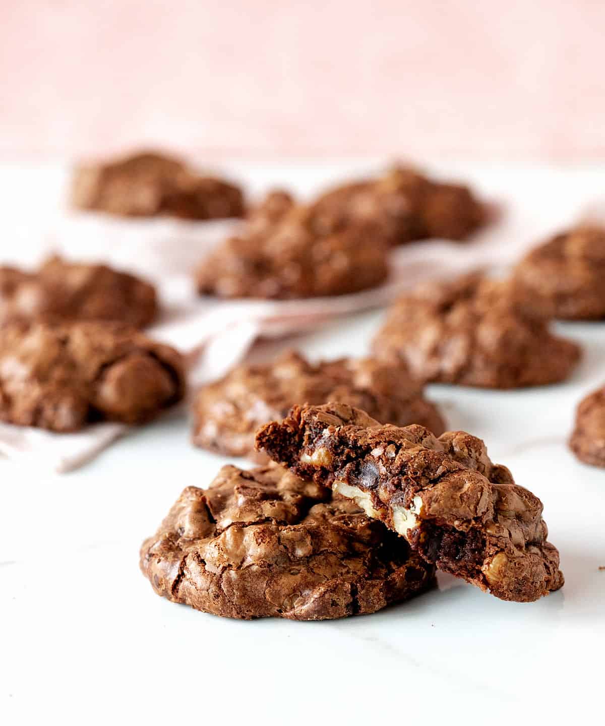 Several chocolate cookies, one bitter, on white and pink surface.