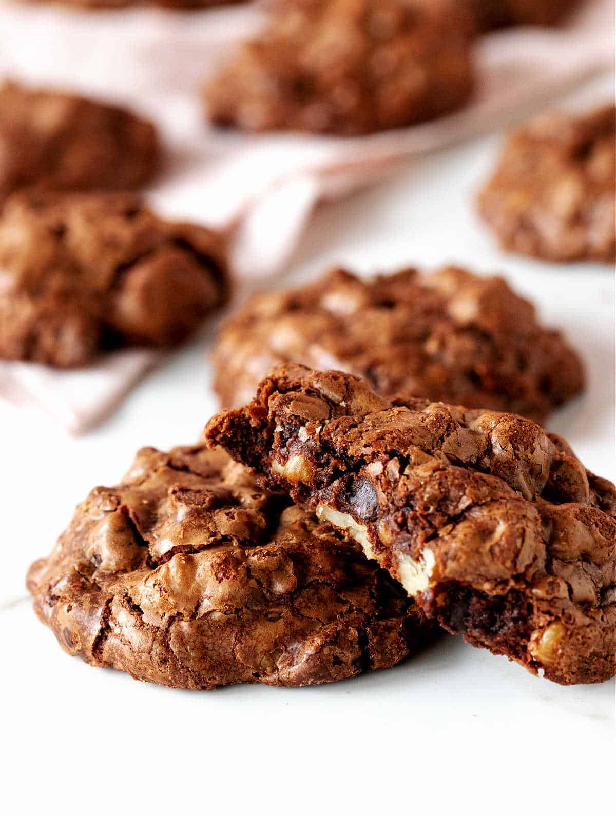 Close up of half a chocolate walnut cookie with several others whole on white pink background.