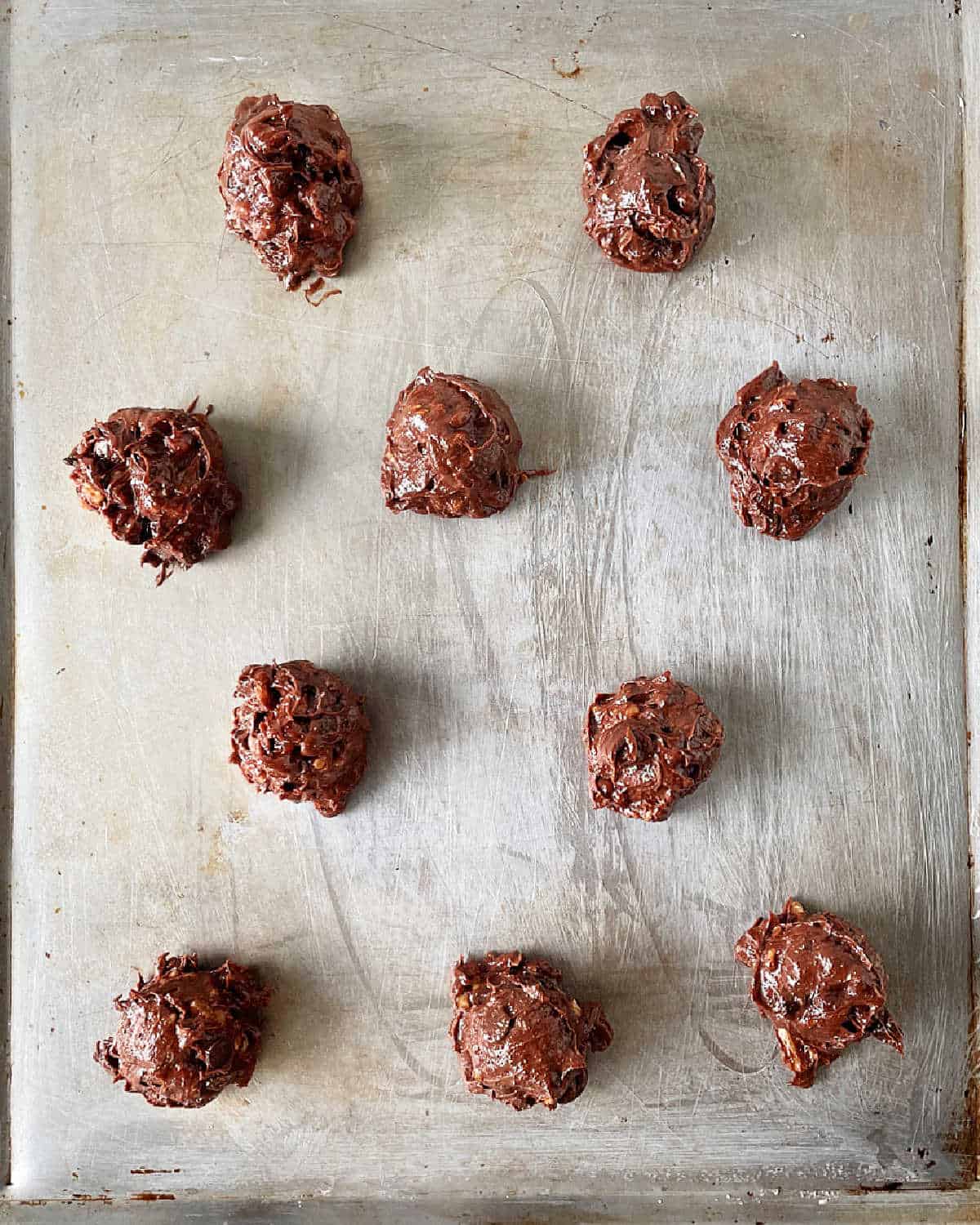 Unbaked chocolate walnut cookie mounds on a metal baking sheet.