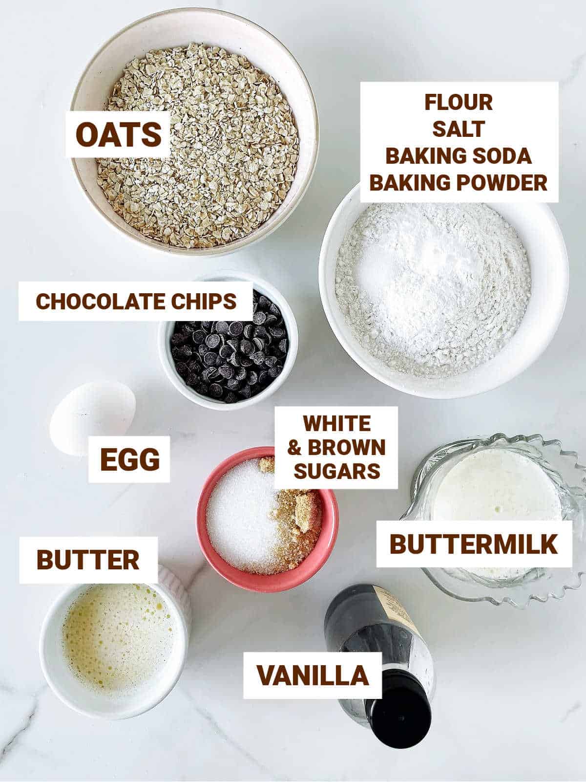 Ingredients for oatmeal chocolate chip muffins in bowl on a white marbled surface.