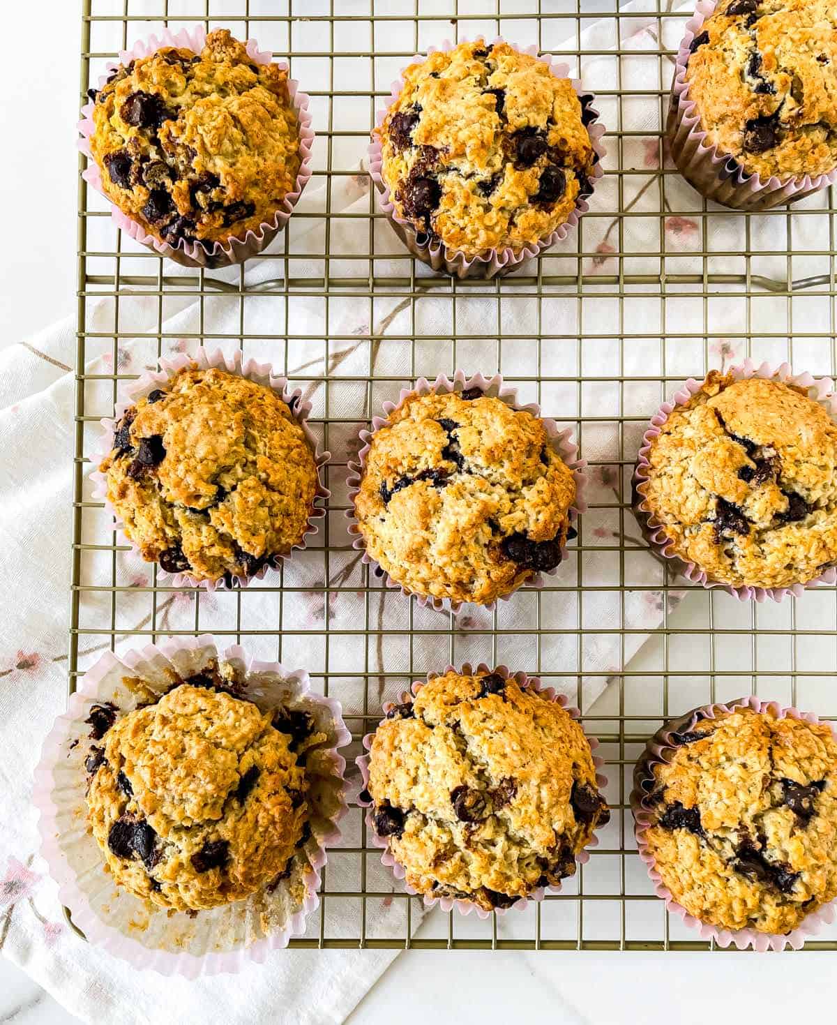 Top view of several oatmeal chocolate chip muffins on a cooling rack over a kitchen towel