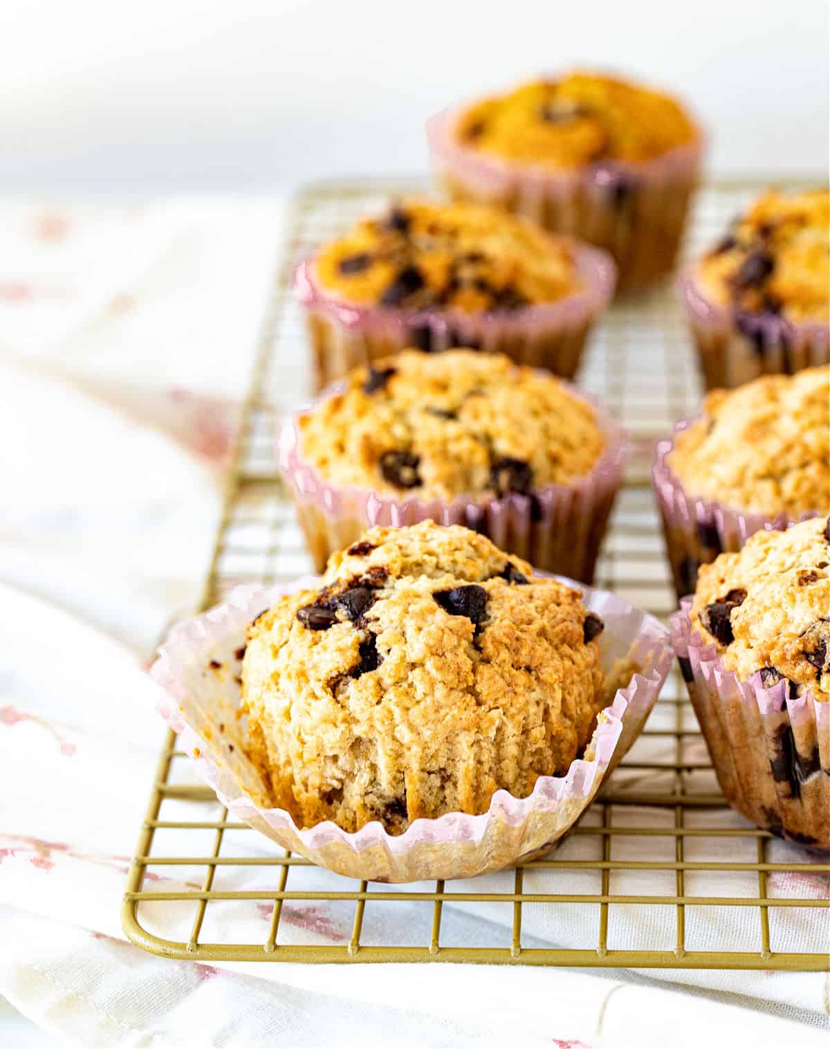 Rows of oatmeal chocolate chip muffins on a golden wire rack.