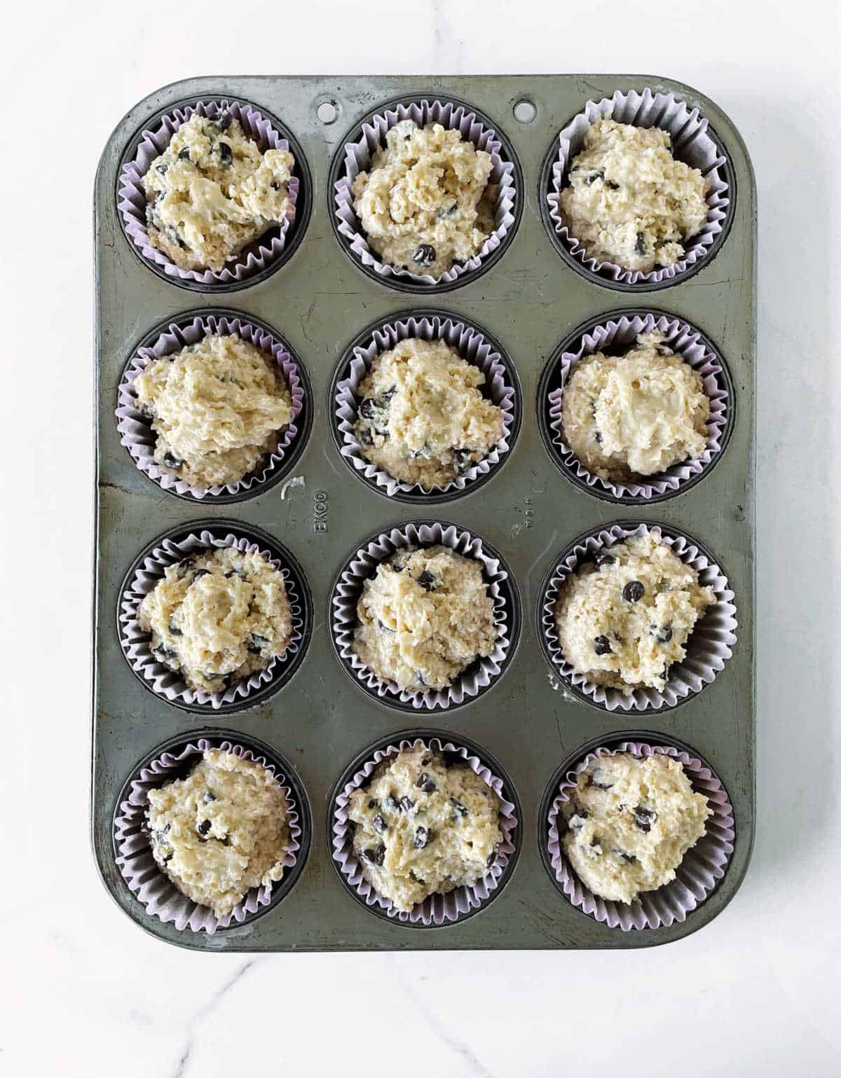 Top view of metal muffin pan with unbaked oatmeal muffins, white surface.
