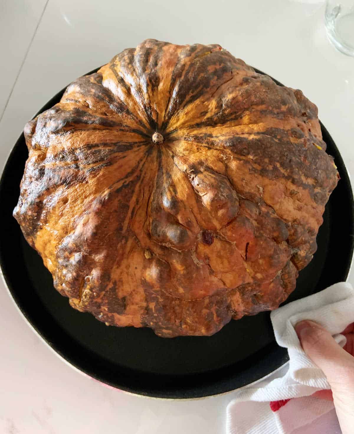 Whole baked pumpkin on black round pan, whitish surface