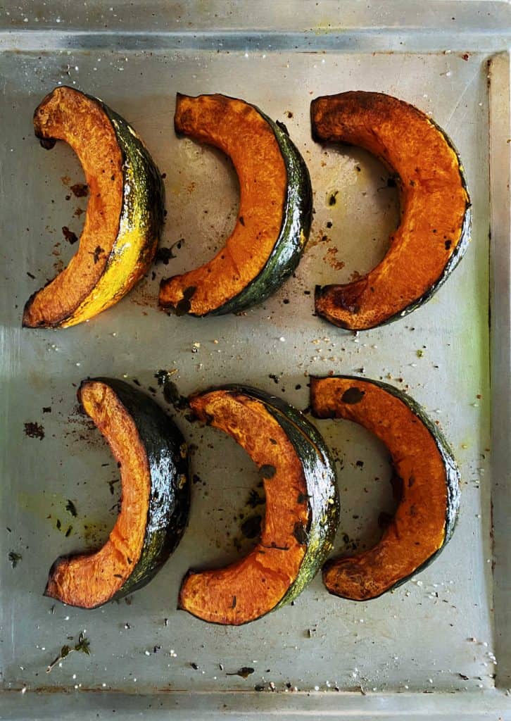 Six baked pumpkin wedges on metal baking sheet