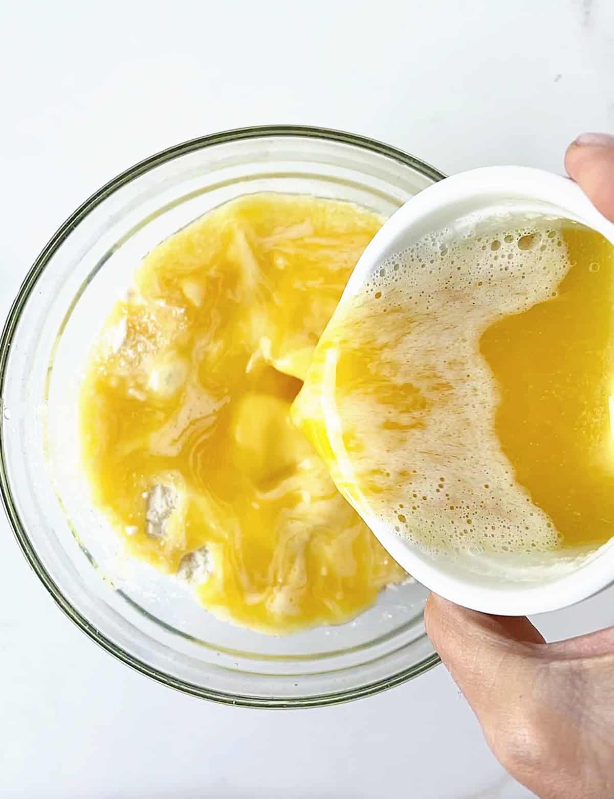 Melted butter being poured into a glass bowl on a white surface. 