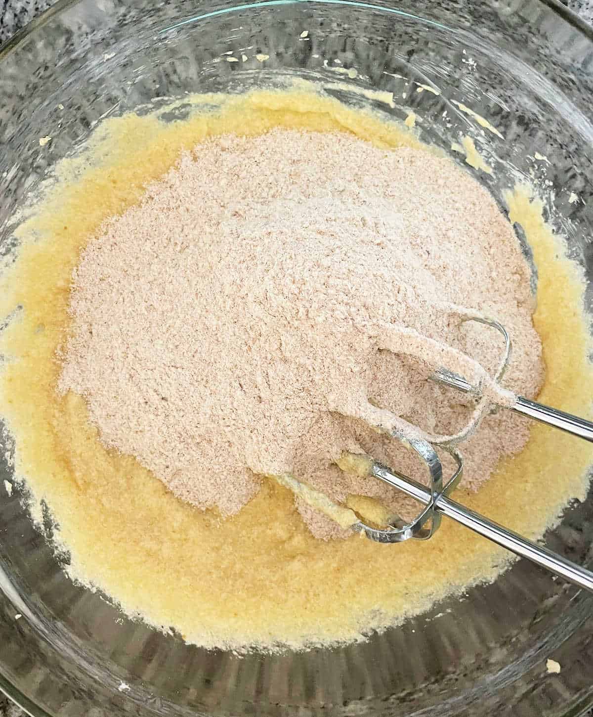Whole wheat flour added to applesauce bread batter in a glass bowl on a grey surface.