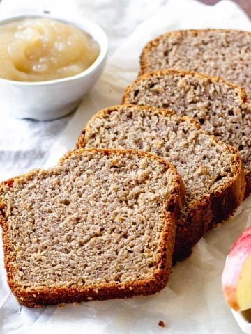 Slices of applesauce bread on a white cloth. Small bowl of applesauce and apple slices.