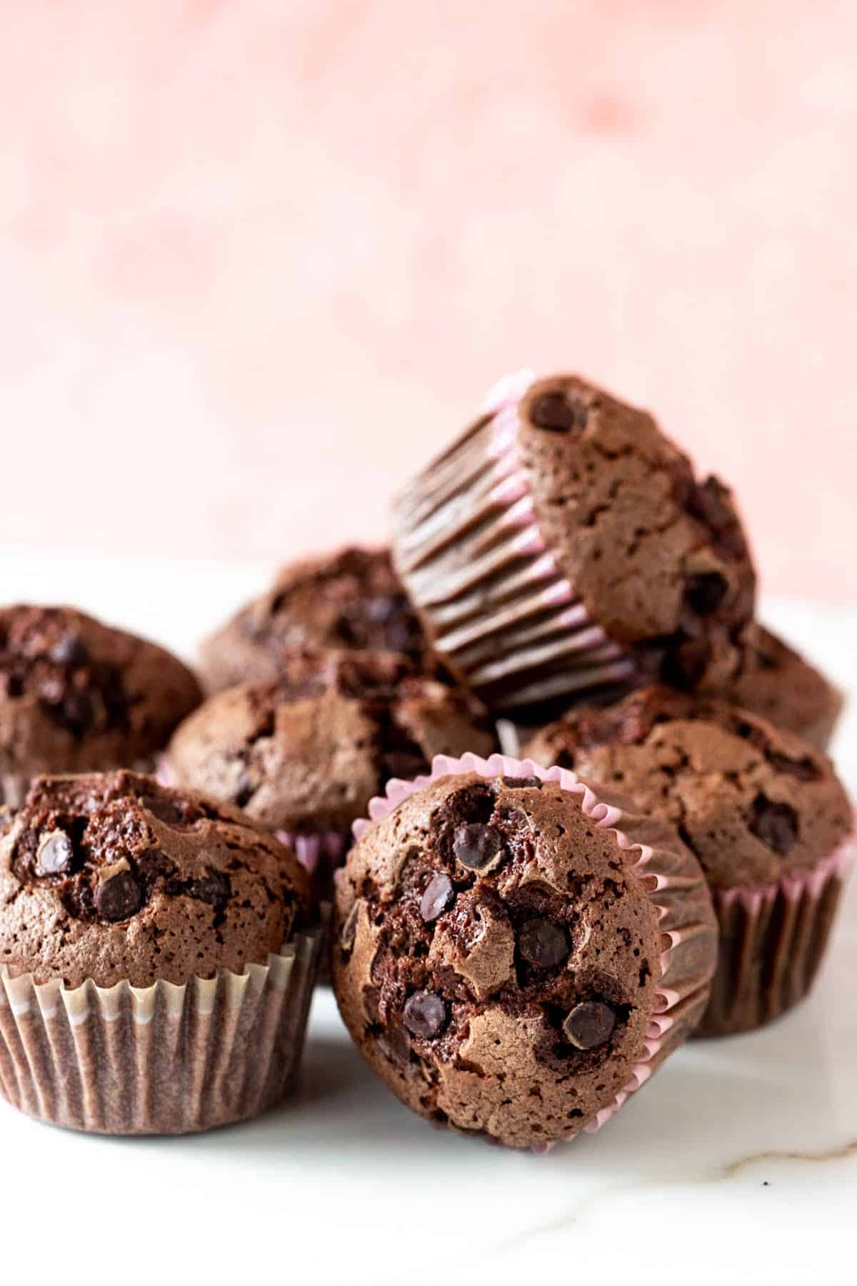 Several whole chocolate muffins in paper liners with white and pink background