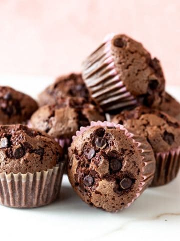 Close up of several chocolate muffins in a mound; white and pink background