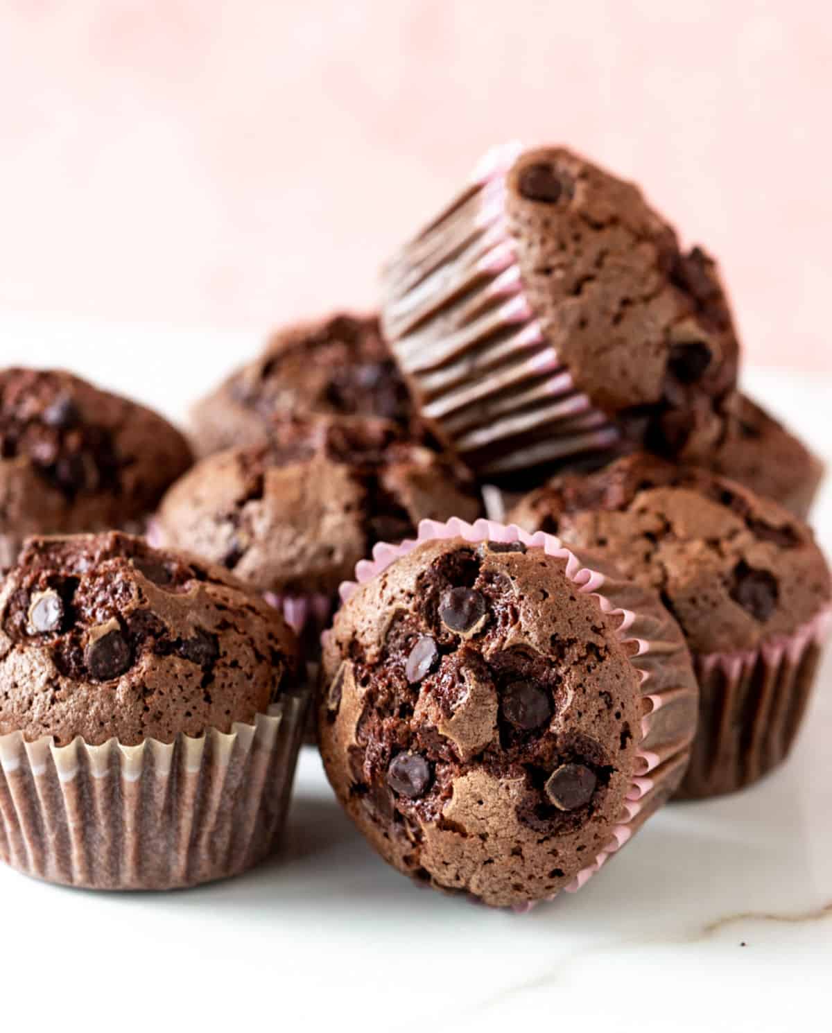 Close up of several chocolate muffins in a mound. White marble surface and pink background.