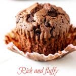 A chocolate muffin in an opened paper liner on white marble; pink brown text overlay