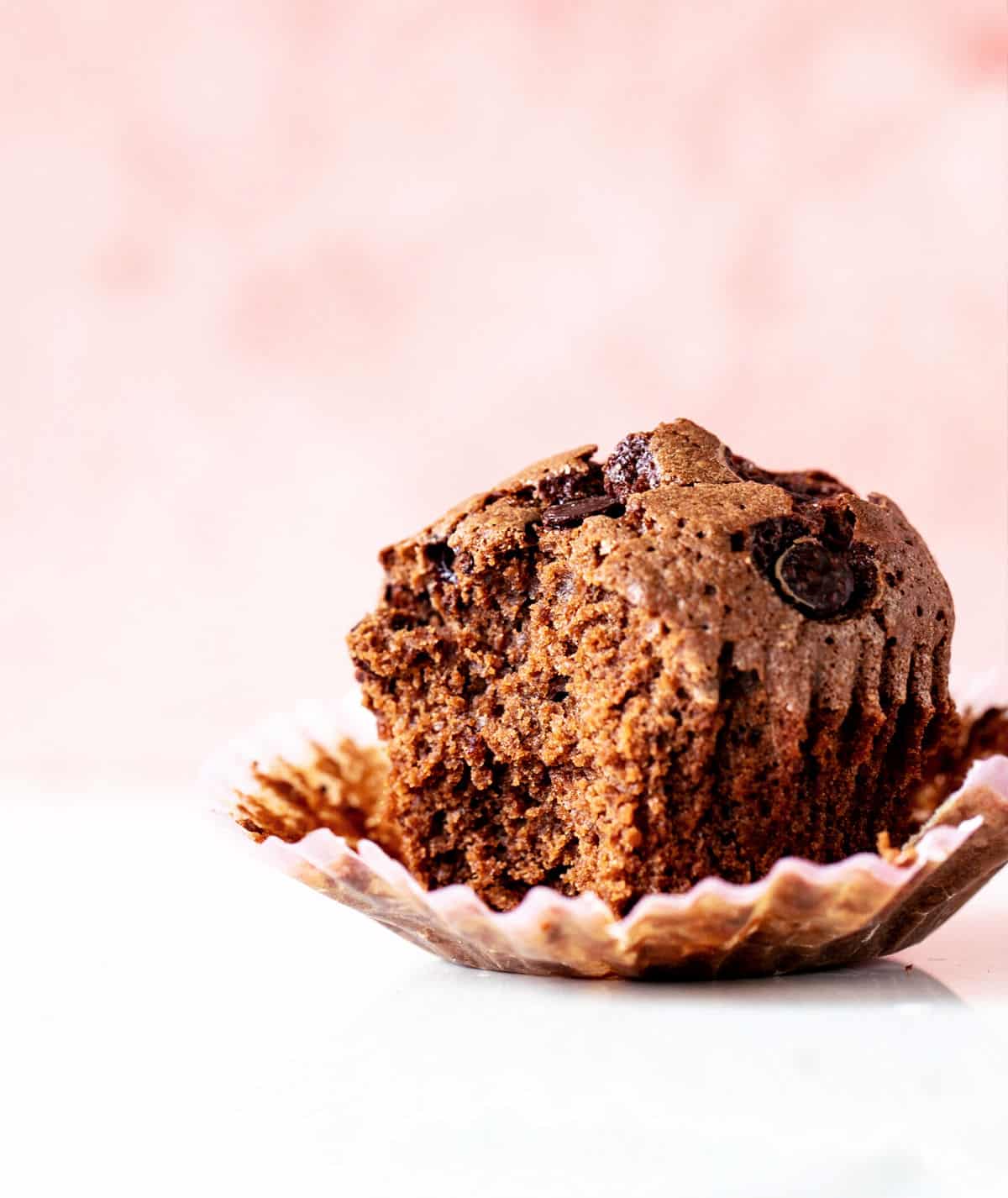 Eaten chocolate muffin in paper liner, white surface and pink background.