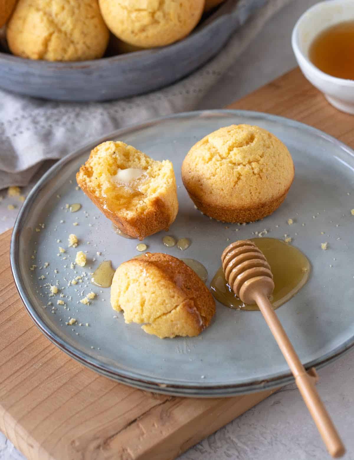 Bluish plate with whole and halved cornbread muffins with honey.