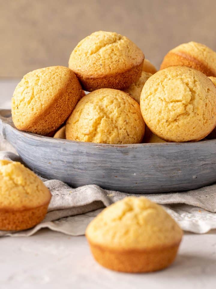 Several cornbread muffins on bluish grey bowl, grey beige surface and background