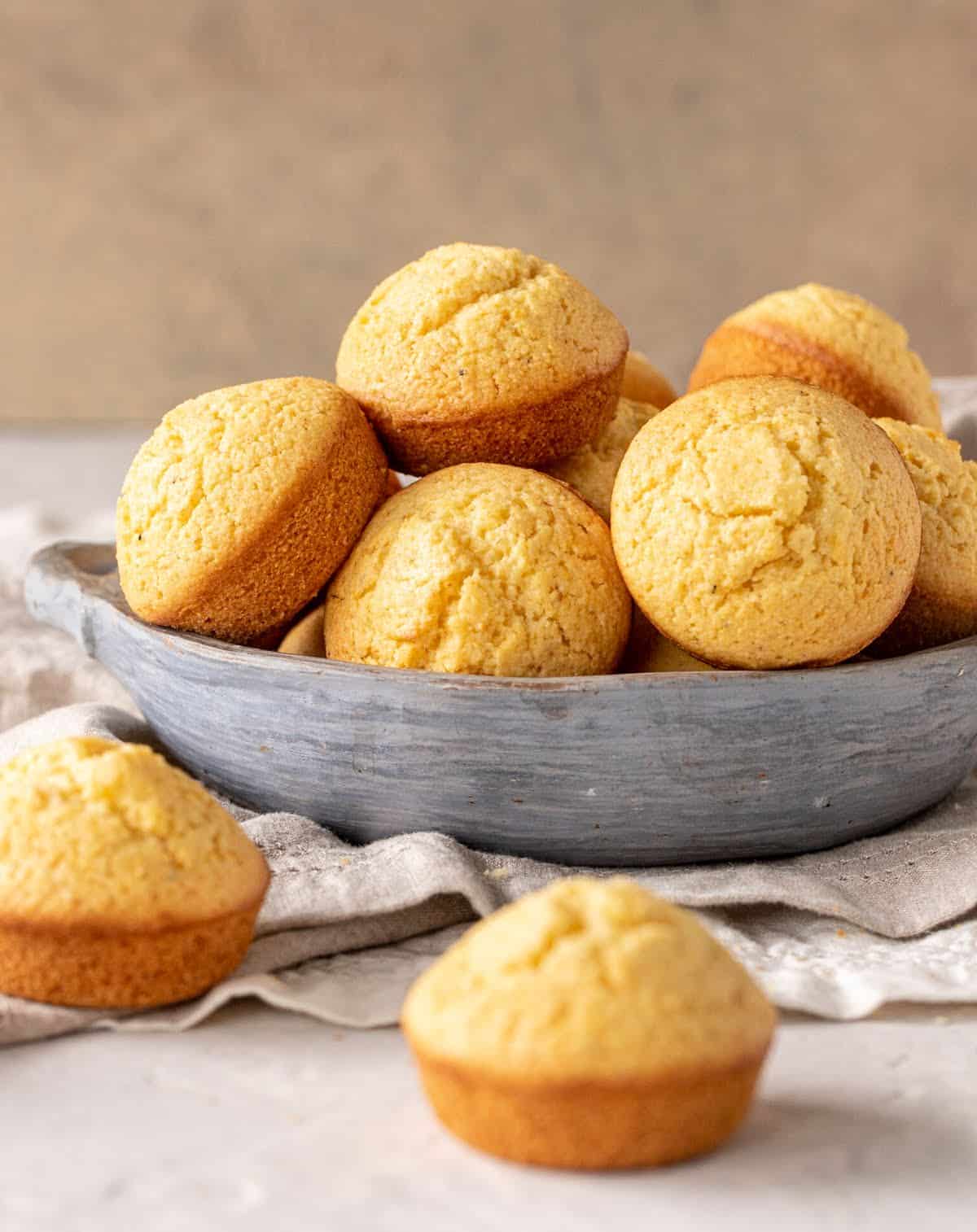 Grey bowl with cornbread muffins, beige napkin and background