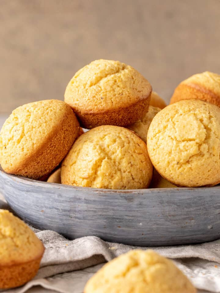 A grey bowl with a pile of cornbread muffins. Beige background.