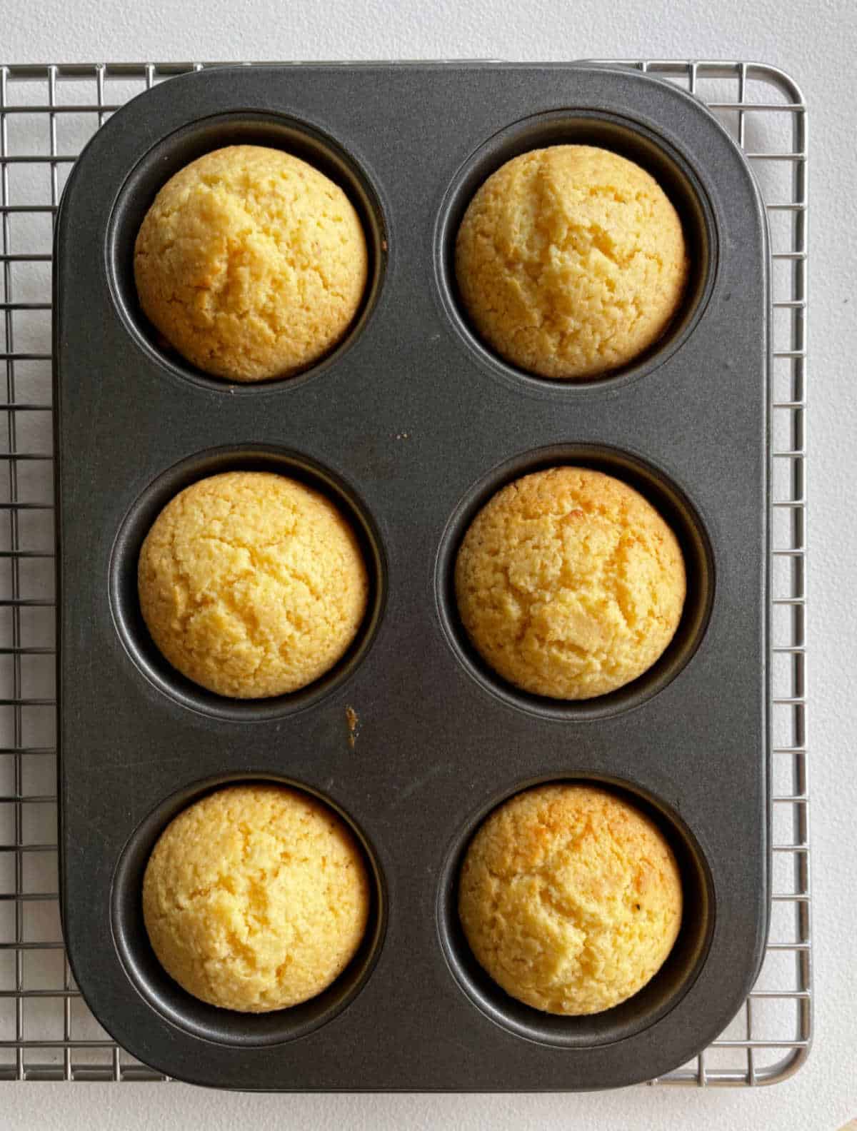 Top view of baked cornbread muffins in a dark metal muffin tin.