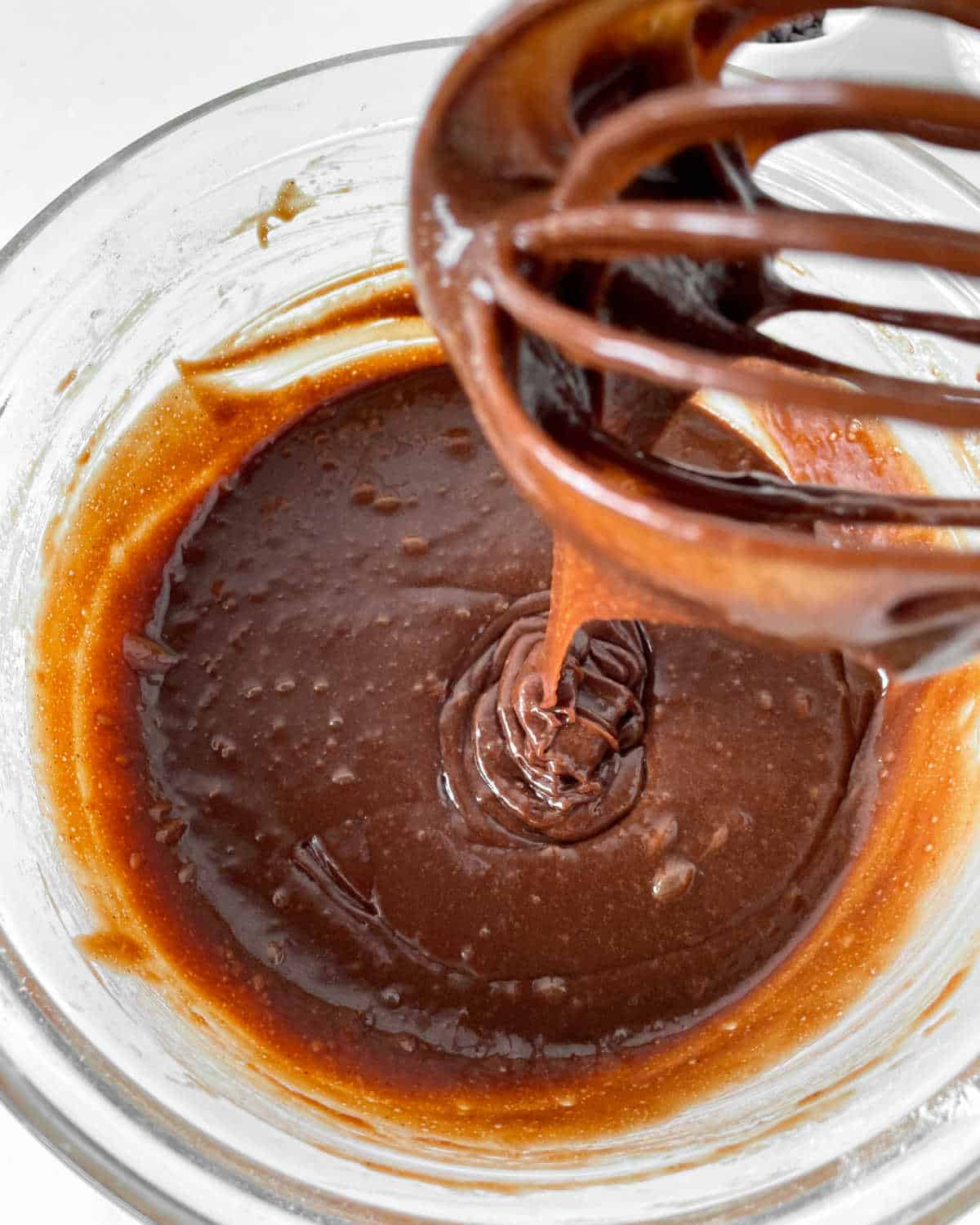 Chocolate muffin batter in a glass bowl and pouring from a whisk.