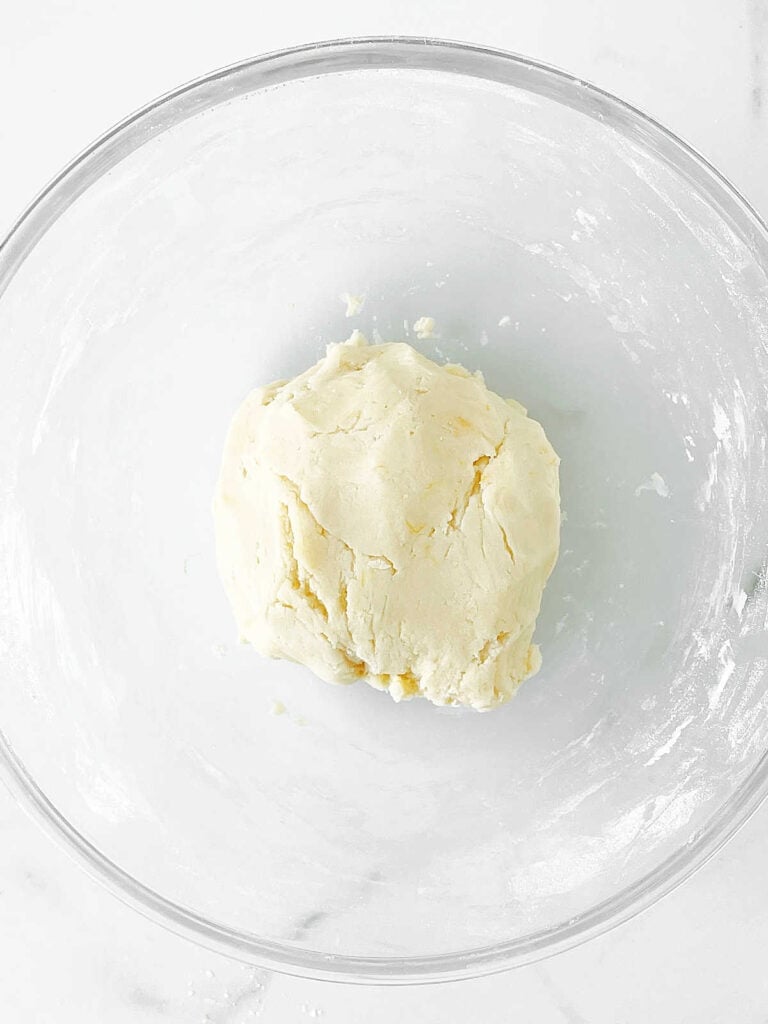 Glass bowl on white marble with shortbread cookie dough ball. Top view.