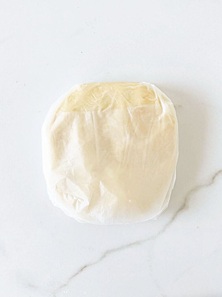 Wrapped shortbread cookie dough on a white marbled surface.