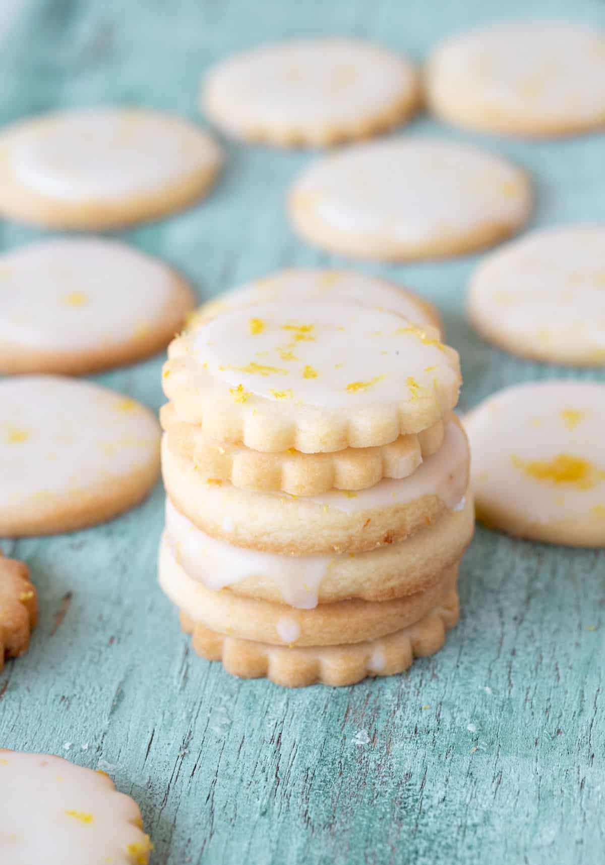 Stack of lemon glazed cookies, and individual ones on green wooden surface