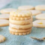 A stack of lemon cookies on greenish wood board, several cookies in background