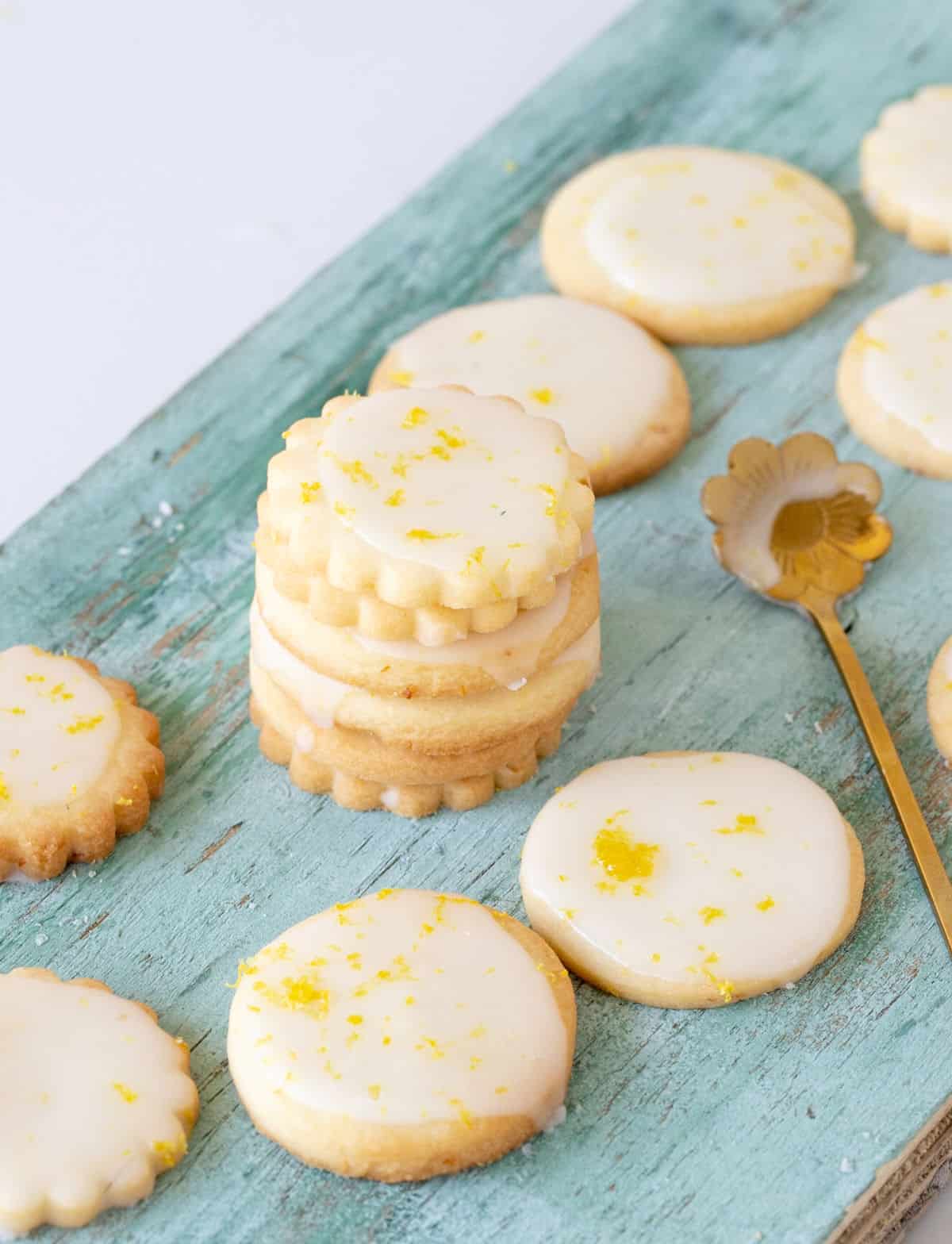 Several glazed cookies stacked and flat on a green wood surface, a gold spoon.