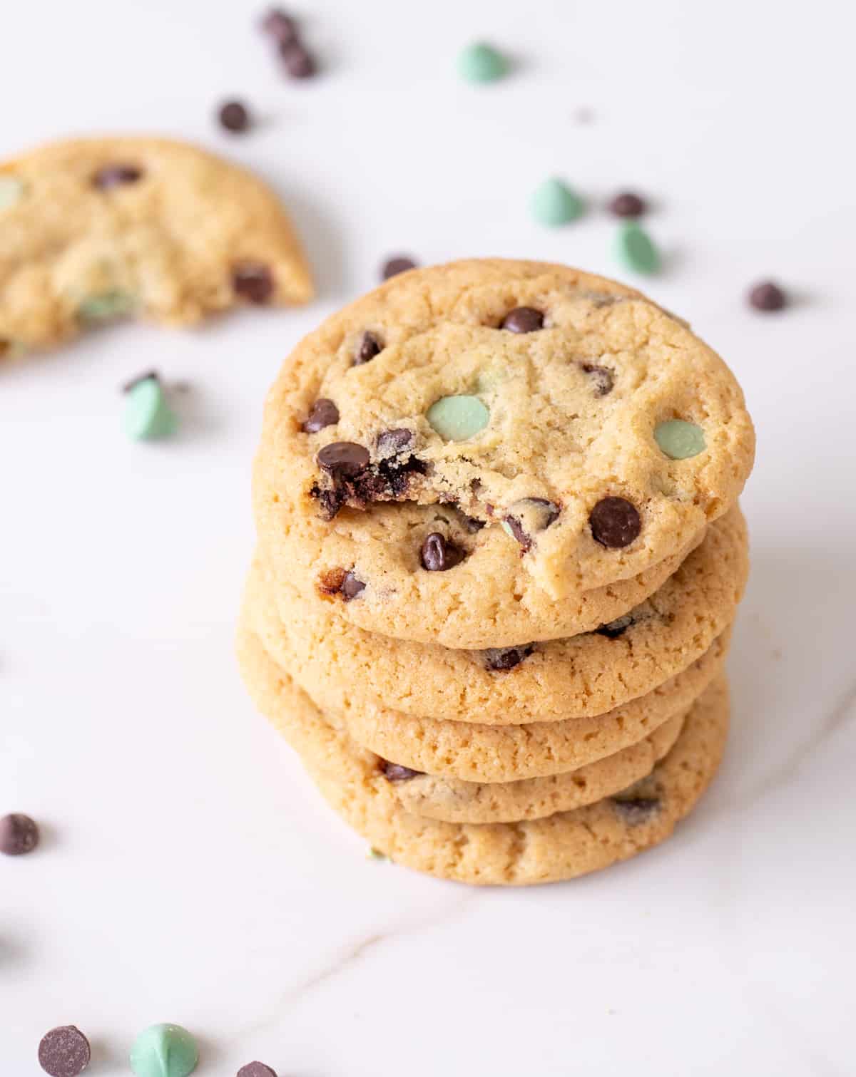 Stack of chocolate and mint chip cookies on white marble, loose chips around