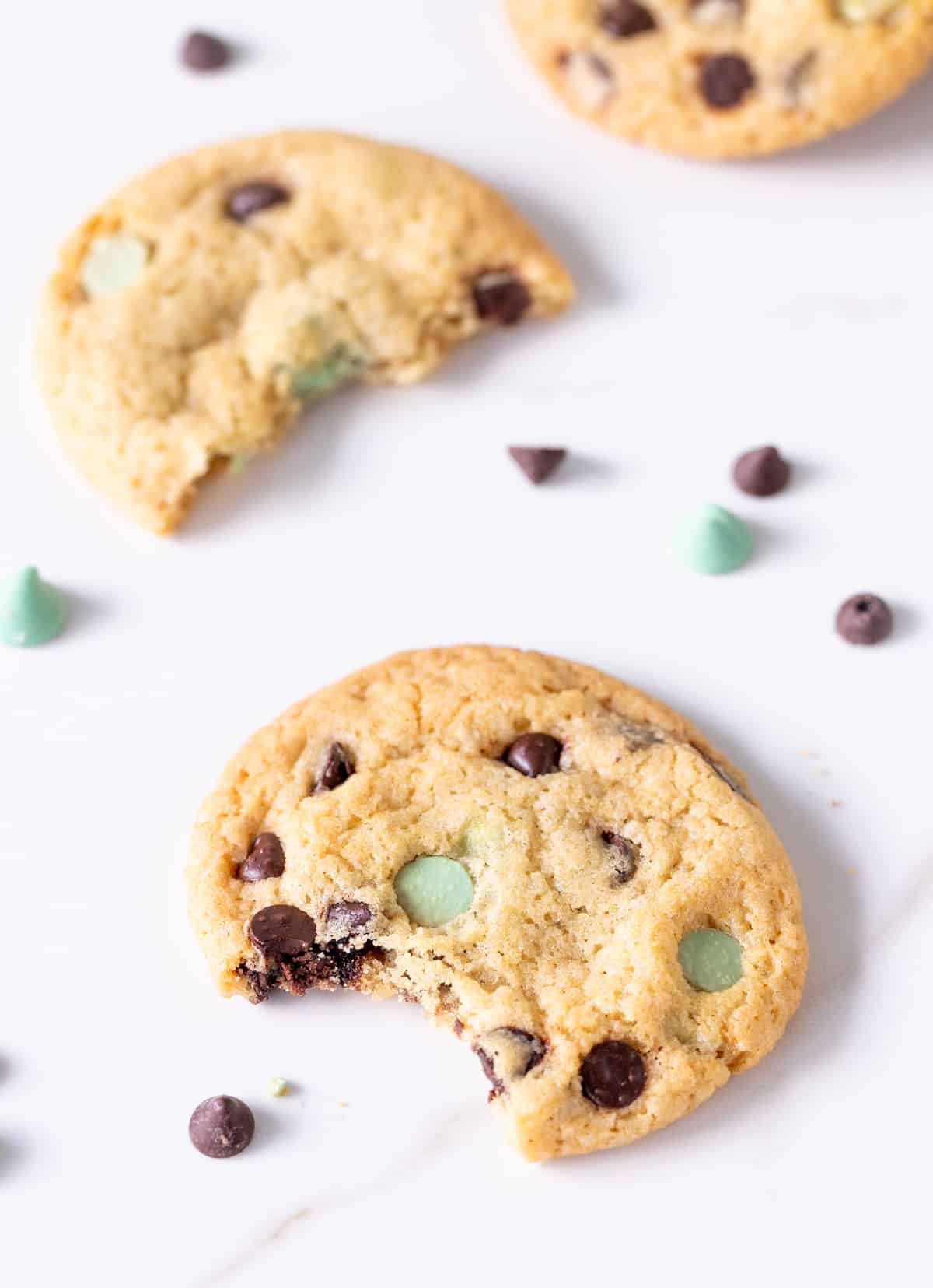 Top view of bitten mint chocolate chip cookies on white marble surface