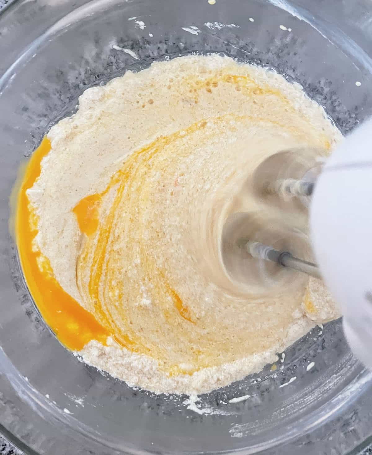 Beating egg into cake batter in a glass bowl on a grey surface. 