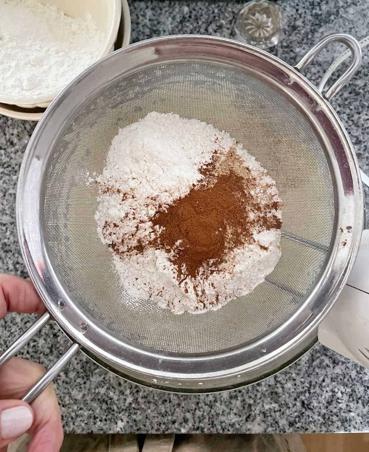 Sifting flour and spices over bowl on a grey marble surface.