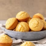 Grey bowl with pile of cornbread muffins. Beige background.