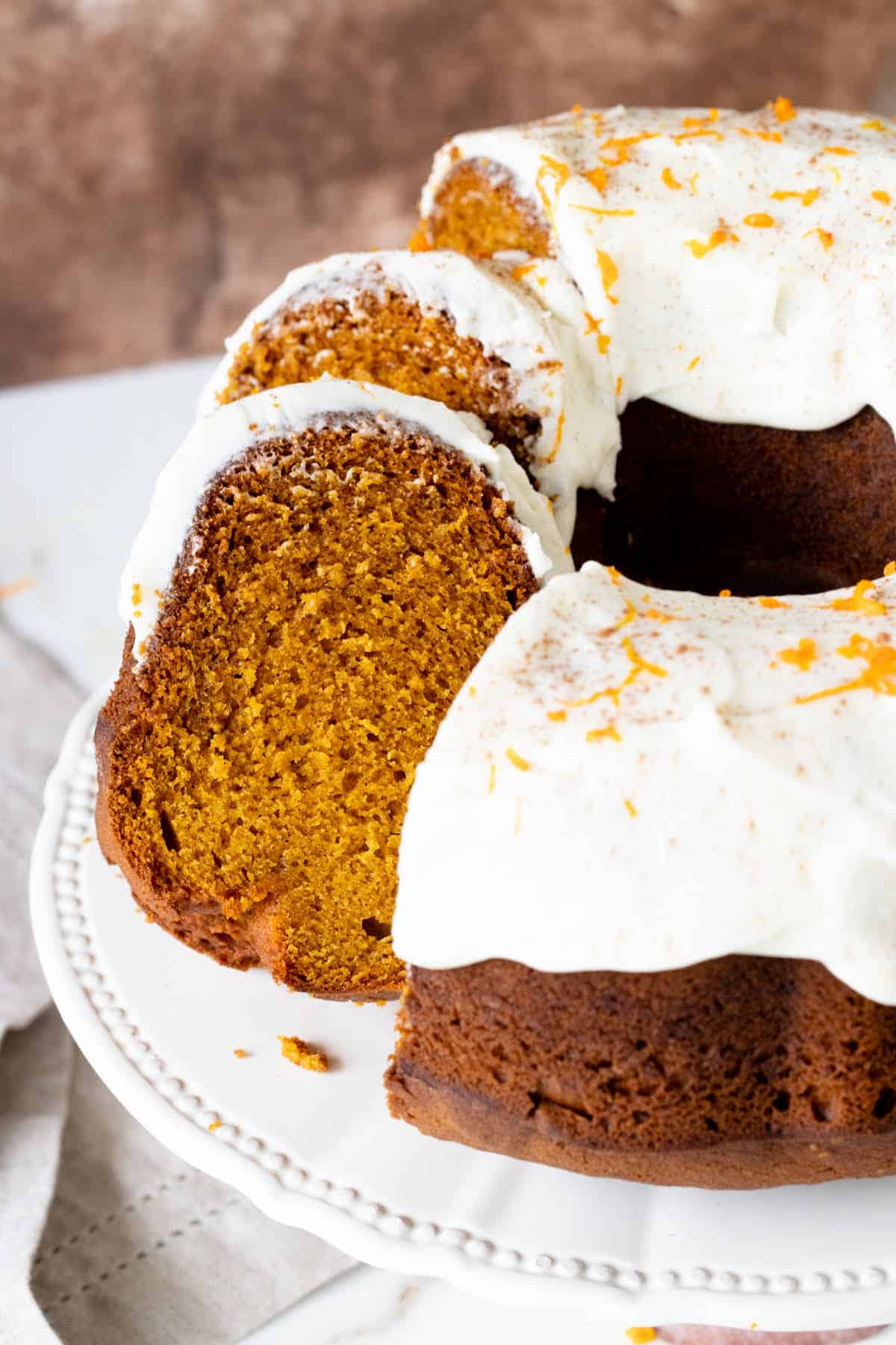 Close up of frosted pumpkin bundt cake in cake stand, cut slices